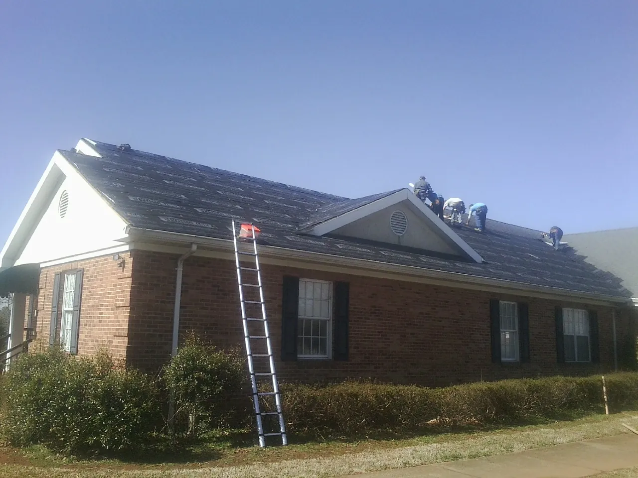 Crew tearing shingles off a brick ranch roof with a ladder set — Emergency Roof Repair work by our crew in Servia