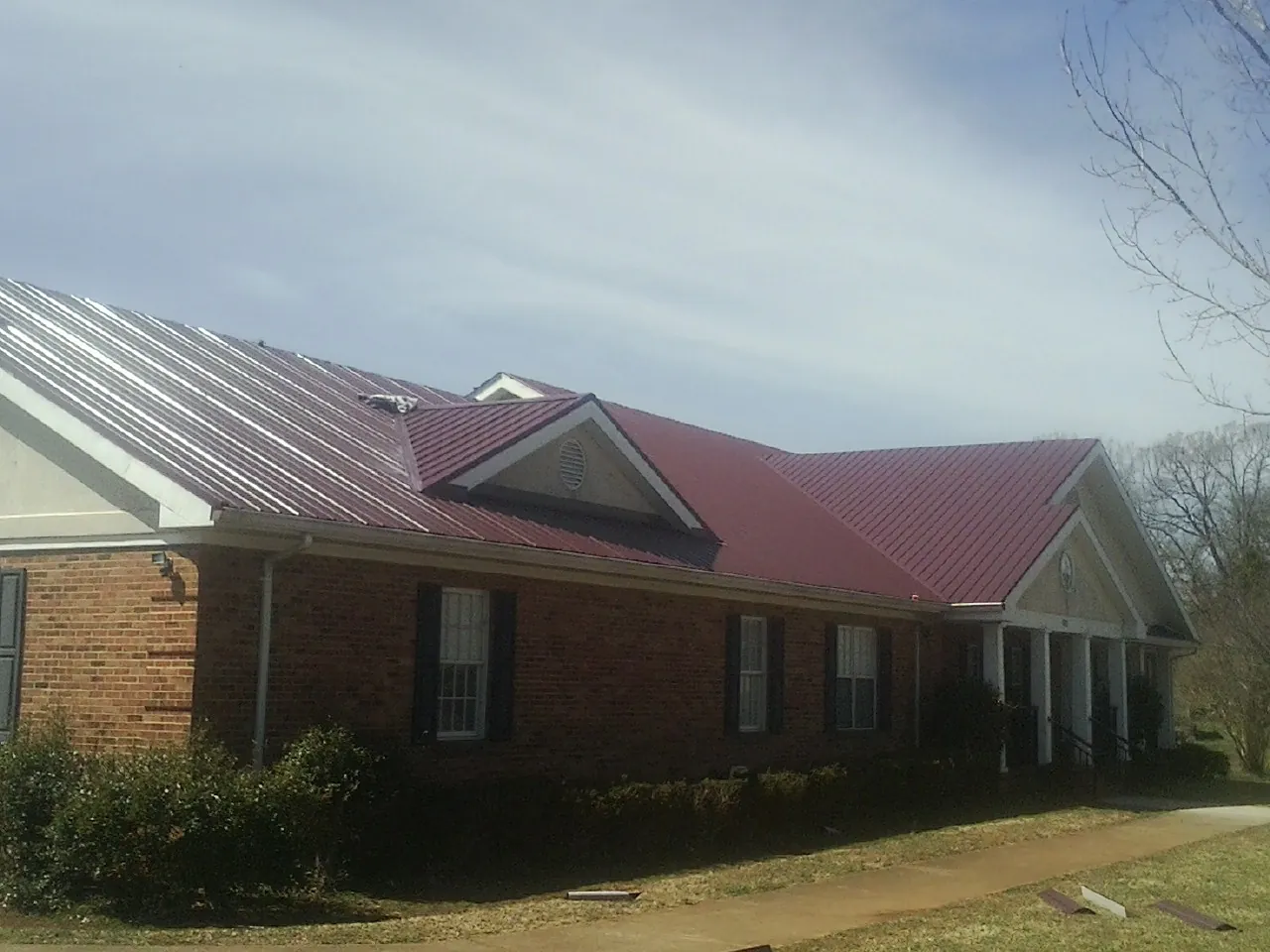 Red metal roof with gabled entries on a long brick building, from a Hail Damage Roof Repair job in Servia