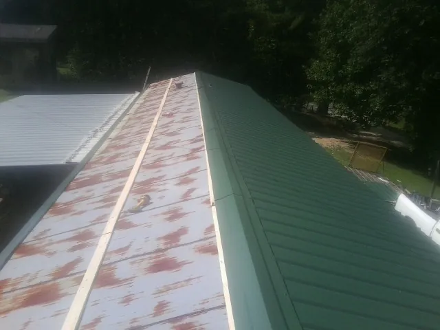 Old rusted panels beside newly installed green metal roofing — Wind Damage Roof Repair by Roofing Brothers in Servia